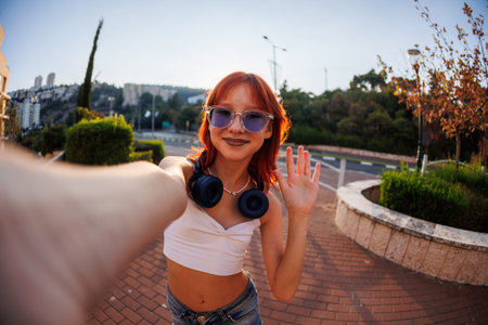 teenage girl with a piercing on her face takes a selfie while walking outdoors on a sunny day....