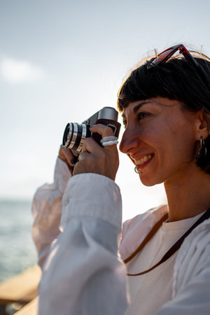 Girl with a camera. Beautiful tourist enjoying the sea view during her vacation and taking pictures...