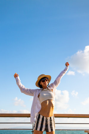 The girl enjoys her vacation. A slender woman stands on the embankment near the sea and enjoys the moment. Freedom and joy. Summer vacation by the sea.の写真素材