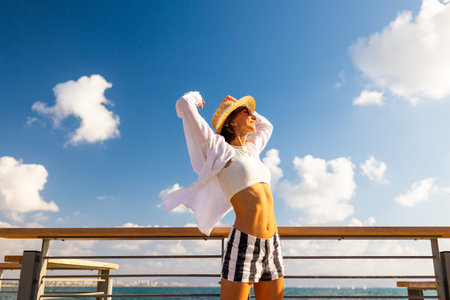 Slender woman stands on the embankment and looks at the ocean. Summer vacation by the sea. Beach lifestyle. Freedom and relaxation on the seashore.の写真素材