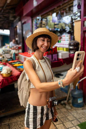 Cheerful smiling woman walking in old city market in arab country taking photos. Girl with phone.の写真素材