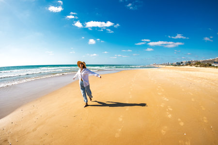 A happy smiling woman on the beach. A beautiful young woman walks along an empty beach. A happy girl strolls along a white sandy beach during summer vacation. Romantic mood.の写真素材