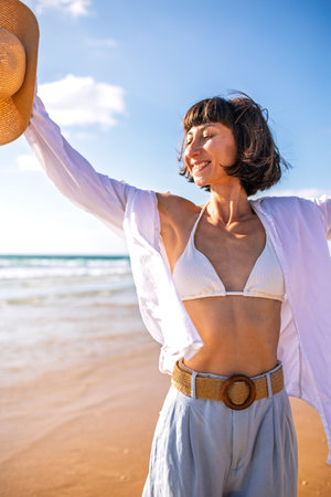 Portrait of a beautiful woman on the beach looking at the camera. A woman stands on the seashore, enjoying the beach breeze. A girl enjoys a moment by the sea. Romantic mood.の写真素材