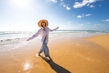 A happy smiling woman on the beach. A beautiful young woman walks along an empty beach. A happy girl strolls along a sandy beach during summer vacation.の写真素材