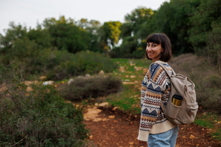 Smiling woman with a backpack hiking in nature. A beautiful female hiker stands on a mountain path and looks at the camera, smiling. Lifestyle, adventure, nature, active life.の写真素材