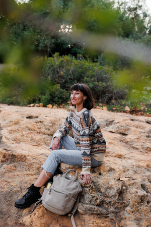 Active lifestyle. A young woman in a stylish sweater enjoys a day in the mountains, sitting on the rocks. hiking and walking.の写真素材