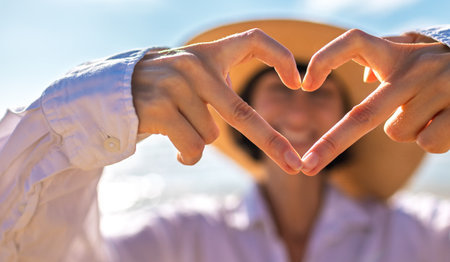 A girl made a beautiful heart with her finger. A cheerful girl makes a heart shape with her hands against a backdrop of sea and sky. Romantic mood.の写真素材