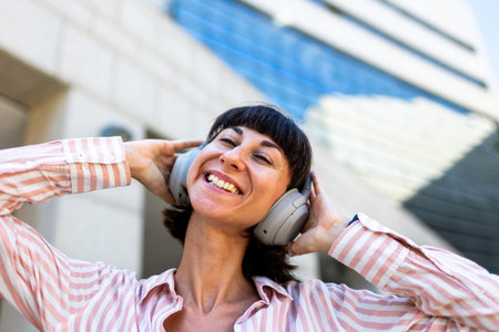 A happy woman, relaxed and carefree, walks down the street, listening to music on headphones and...