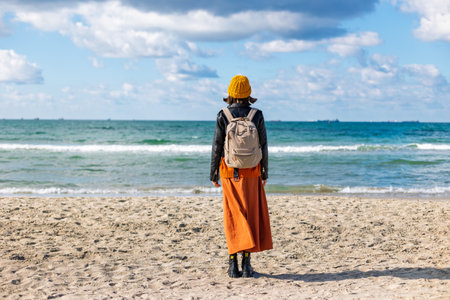 Traveling woman with backpack on the beach in cold weather. Stylish woman enjoying a walk near the sea on a sunny day. girl with a backpack.の写真素材