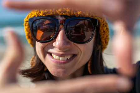 girl smiles. portrait of a cheerful girl on the beach on a sunny day. stylish woman in a hat and jacket enjoys going to the beach on a sunny day. Lifestyle, travel, tourism, nature, active life.の写真素材