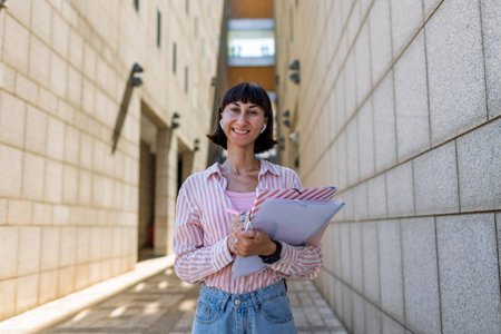 Confident professional with clipboard standing on a sunny urban street. Elegant professional outside the office, happy lady executive in the city.の写真素材