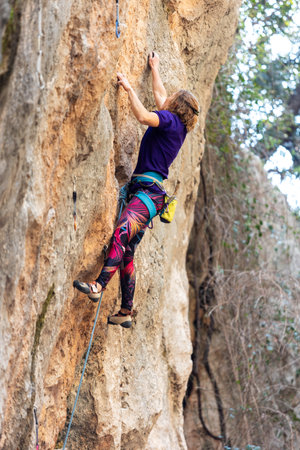 A woman climbs a rock, a strong girl trains strength and endurance, extreme sport, rock climbing on natural terrain, a rock climber climbs. Sport and beauty.の写真素材