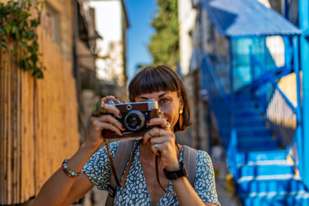 An attractive tourist with a camera. A beautiful woman with a camera takes pictures of beautiful places. The girl raises the camera to her face and takes a photo. Travel and adventure.の写真素材