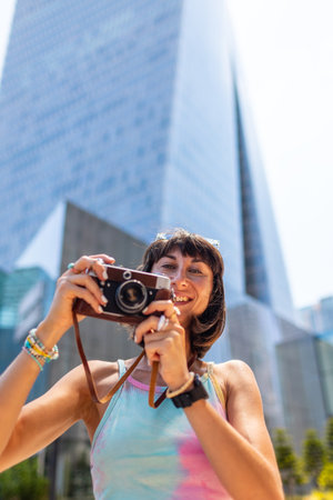 Creating a social media contact. Girl with a camera against the backdrop of modern buildings. Stylish tourist with a camera taking pictures. Girl with a camera.の写真素材
