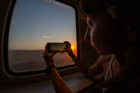 Young woman travels by train and creates content for social networks. Girl takes photos from the window of a moving train. Train travel.の写真素材