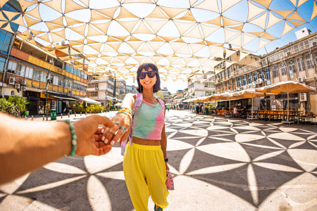 A girl traveler holds a guy's hand and walks along the street. Vacation, tourism.