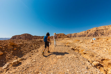 Two active backpackers stroll through the desert against a blue sky. Mother and child on a hike. Summer camp. Timna National Park. The child is actively spending time. Trekking and hiking.の写真素材