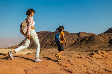 A boy with a backpack and a map walks next to his mother through the desert. Family trekking. Timna National Park. The child is actively spending time. Trekking and hiking.の写真素材