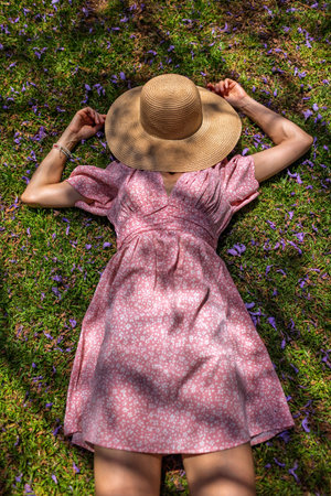 Young woman lying on the field in green grass and flowers. Hat covering her face. Summer mood. Girl...