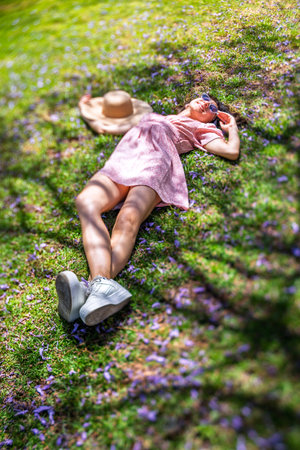 Young woman lying on the field in green grass and flowers. Hat covering her face. Summer mood. Girl...