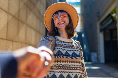 girls and her friend are walking in the city, a happy young woman holding a guy's hand and smiling...