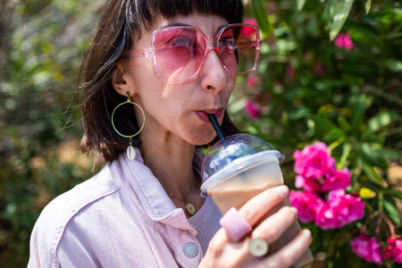 A beautiful woman enjoys her morning coffee and smiles. She's relaxing, taking a break. A happy young lady walks down the street, drinking take-out coffee.の写真素材