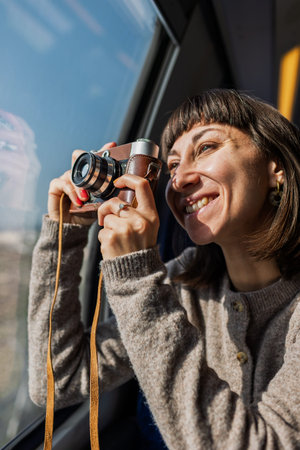 A beautiful, happy young woman takes a photo with a vintage analog camera from a train window....