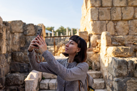A girl is filming content. A stylish tourist strolls among ruins with a backpack, photographing...