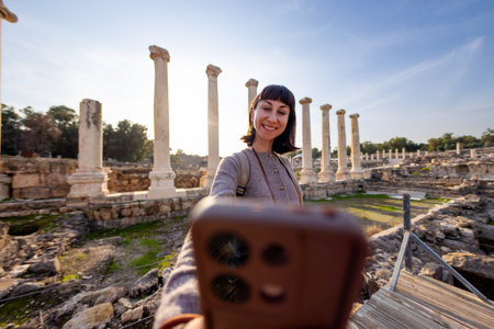 A girl is filming content. A stylish tourist strolls among ruins with a backpack, photographing landmarks for her blog and social media. A tourist near ancient stone ruins in Israel. Beit She'an.の写真素材