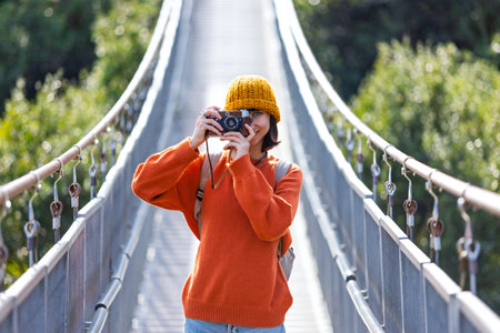 Travel and photography. A young woman with a camera and a backpack walks along a suspension bridge....