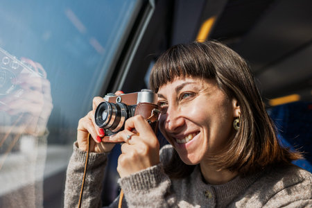 A beautiful, happy young woman takes a photo with a vintage analog camera from a train window....