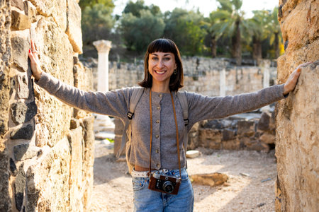 A young woman with a backpack and a camera explores ancient ruins. The woman films videos for travel blogs, documentaries about culture, and tourism. creates content for the blog. Beit She'an, Israel.の写真素材