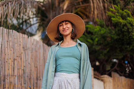 Close-up portrait of a traveling brunette woman wearing a hat, stylish summer clothes. Cheerful young woman smiling on the beach during summer vacation. Happy girl.の写真素材