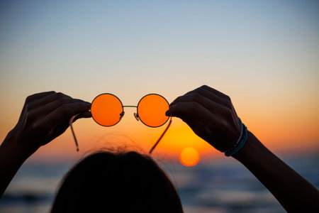 girl holds sunglasses in her hands. a young girl enjoys her holiday by the sea. girl near the sea.の写真素材