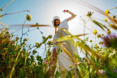 Summer mood. a young and cheerful girl posing against a background of blue sky and flowers. girl dancing among flowers. spring fashion.の写真素材