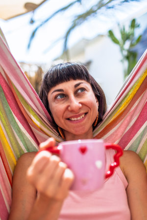 Summer mood. girl drinking morning coffee sitting in a hammock. girl enjoying rest in camping. cup in the shape of a heart.の写真素材