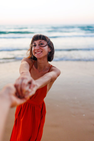 happy young woman pulls guy's hand. girl having fun on the beach. a beautiful girl in a dress walks along the beach, holding a guy?s hand, a romantic walk. walk on the beach.の写真素材