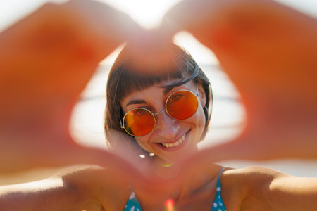 Close-up of a smiling woman making a heart shape with her hands. joyful woman laughs in front of the camera. girl has fun on the beach.の写真素材