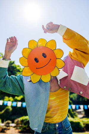 A girl in a cheerful mask is having fun at a summer festival. A charming, cheerful woman in fashionable clothes and a mask creates content for social media. Summer mood. Girl in a mask.