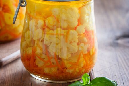 Pickled cauliflower with carrots in glass jars on a wooden table, horizontalの写真素材