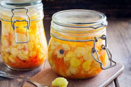 Pickled cauliflower with carrots in glass jars on a wooden table, horizontalの写真素材