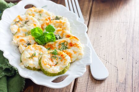 Baked zucchini with cheese slices on a white dish on a wooden table, horizontal, copy spaceの写真素材