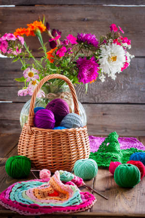 Multi-colored balls of cotton thread for crocheting in a wicker basket on a wooden table and ready knitted napkin made of multi-colored thread, selective focusの写真素材