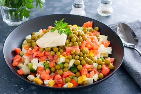 Salad with red fish, Olivier, in a black bowl on the table, selective focusの写真素材