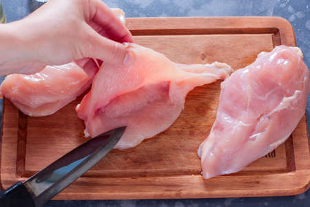 Step-by-step cooking of stuffed chicken breasts in the oven filled with cheese, spinach and garlic, step 3 - cutting the chicken fillet, female hands show how to make chicken pockets, horizontalの写真素材