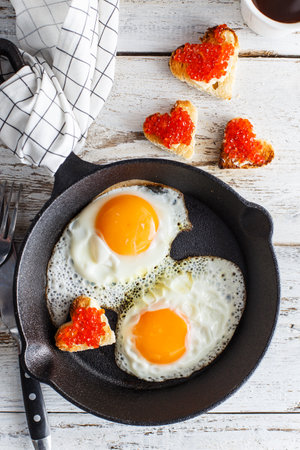 Breakfast with fried eggs in a cast-iron pan with sandwiches with red caviar, top viewの写真素材