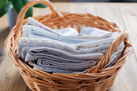 Clean kitchen textiles made of cotton and linen - napkins, towels in a wicker willow basket with two handles on the table, horizontalの写真素材