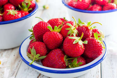 Fresh strawberries in an enamel bowl on a wooden table, selective focusの写真素材