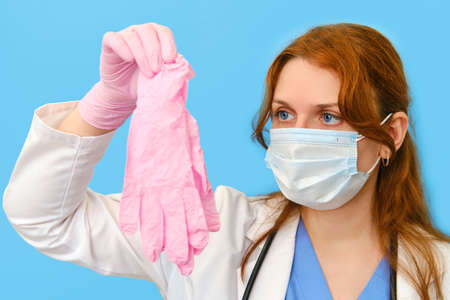 Woman doctor holding pink medical gloves on a blue background, close-up.の写真素材