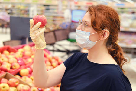 Young woman in a medical mask after quarantine removal buys products in a store. Being in public places during the epidemic of the coronavirusの写真素材